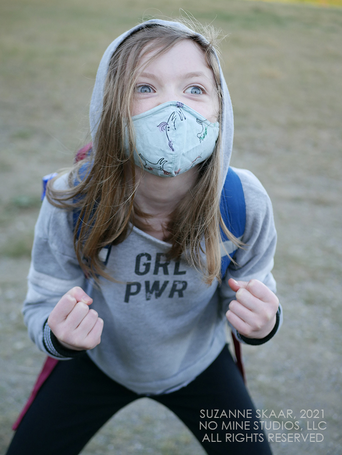 Child wearing gray hoodie which reads "GRL PWR" (Girl Power) crouched, fists raised, and eyes wide. 
