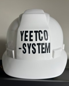 White construction helmet, black stick on block letters which say "Yeetcosystem."